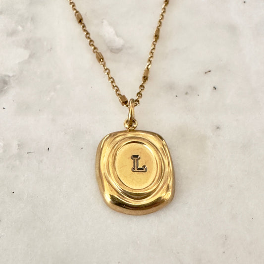 Gold necklace with a pendant featuring the letter 'L' on a marble surface