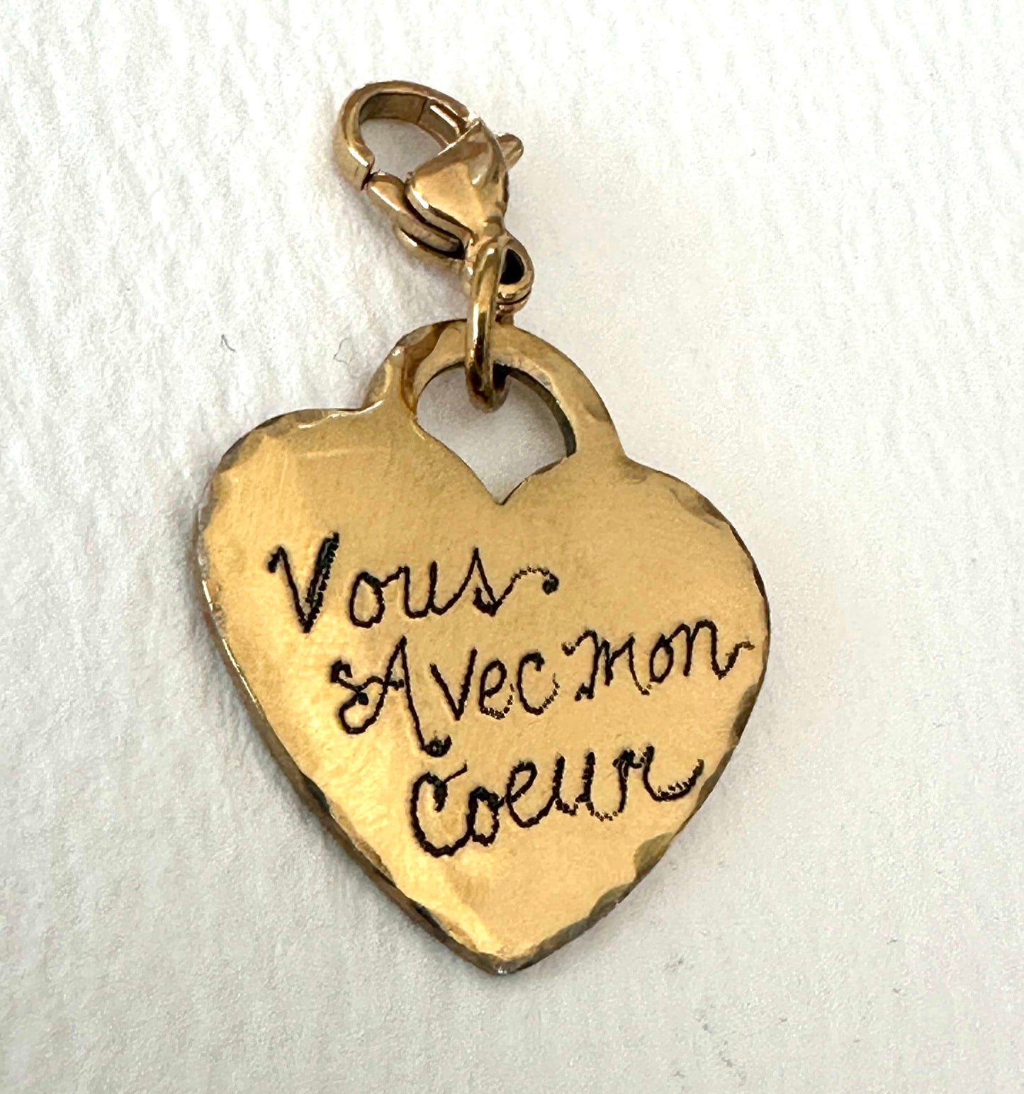 Gold heart-shaped charm with engraved text and clasp on a white background