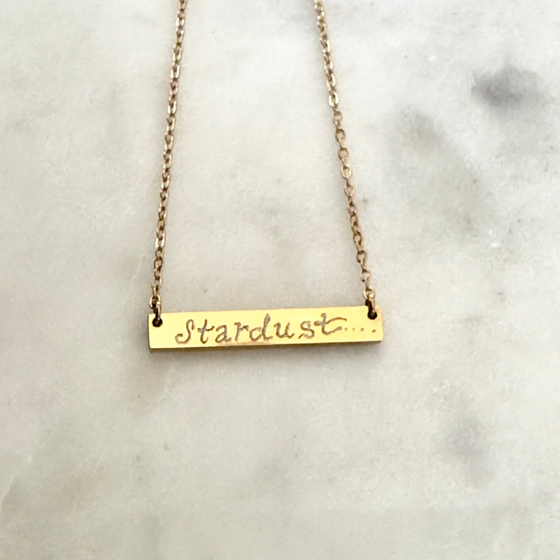 Gold bar necklace with 'Stardust' script on a marble surface