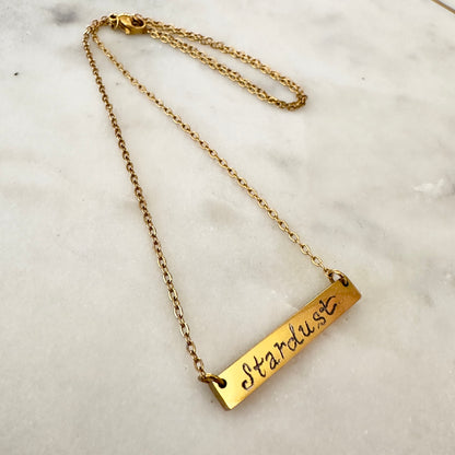 Gold necklace with 'Stardust' pendant on a marble surface
