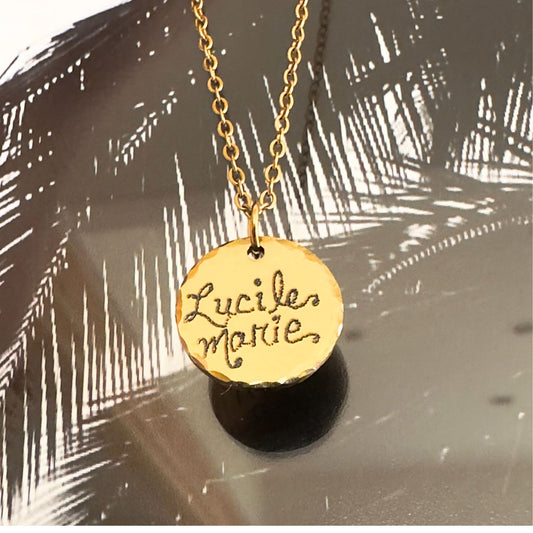Gold necklace with a pendant engraved name in script on a textured surface.