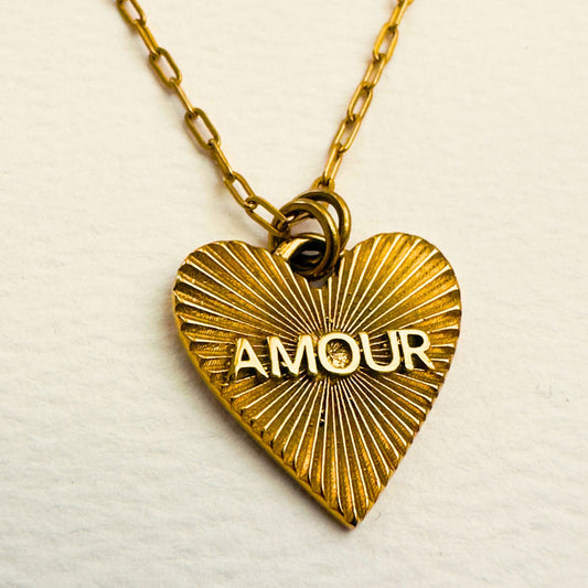 detail photo of gold heart pendant necklace that says amour on a paperclip style chain